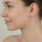 Close-up of an ear wearing a silver dual band half hoop stud earring with a neutral background