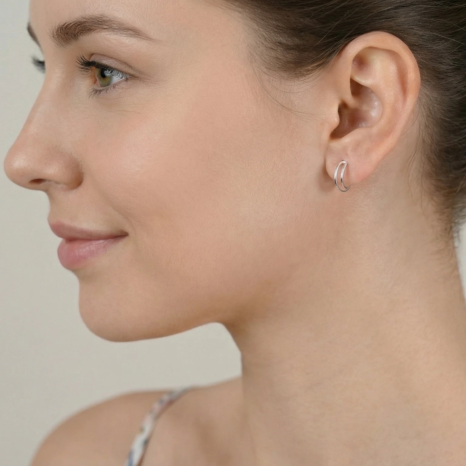 Close-up of an ear wearing a silver dual band half hoop stud earring with a neutral background