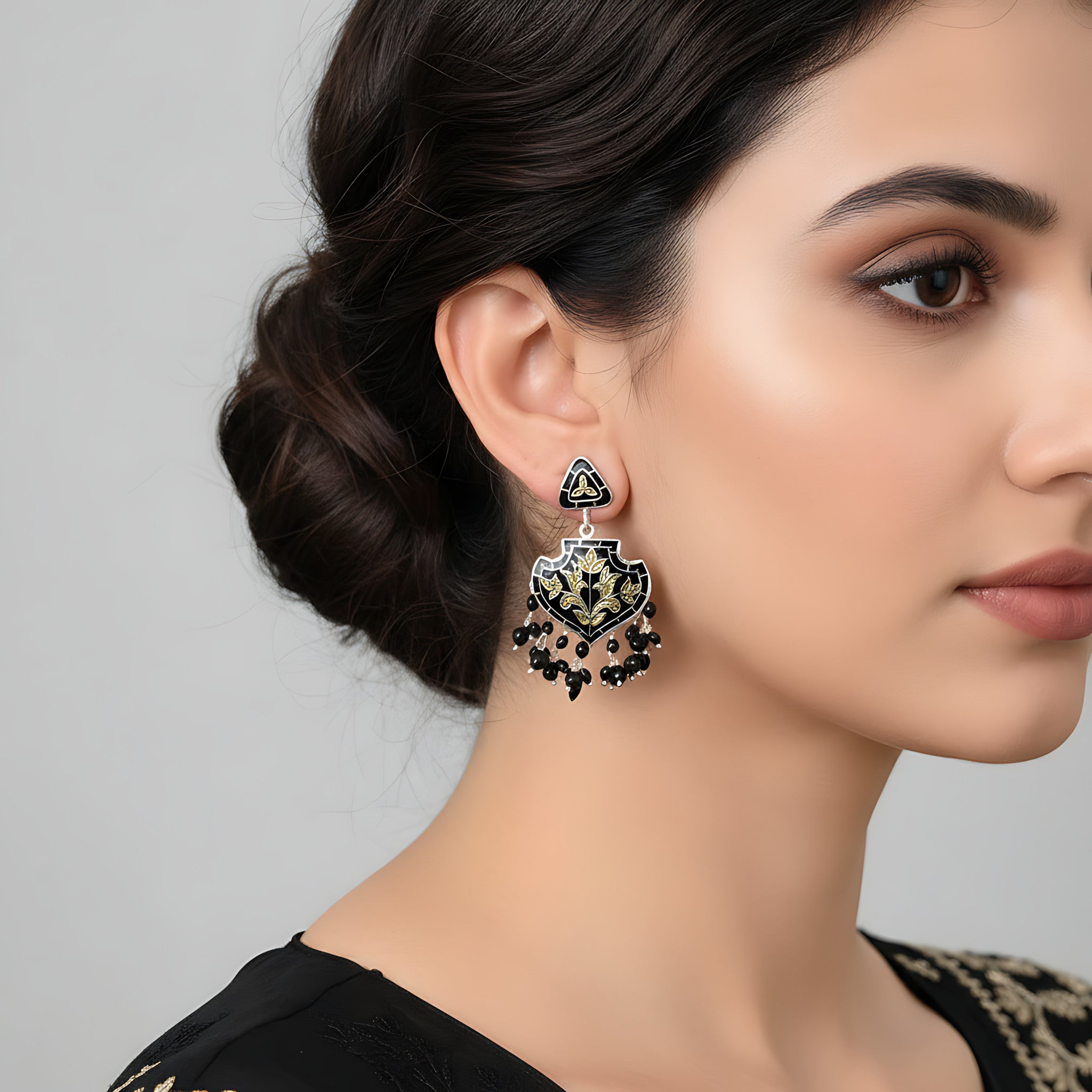 Close-up of a woman wearing an ornate black-gold silver enamel earring against a neutral background