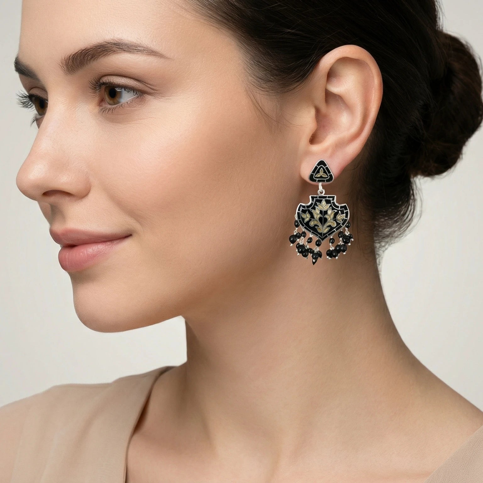 Woman wearing a decorative black-gold silver enamel earring with a neutral background