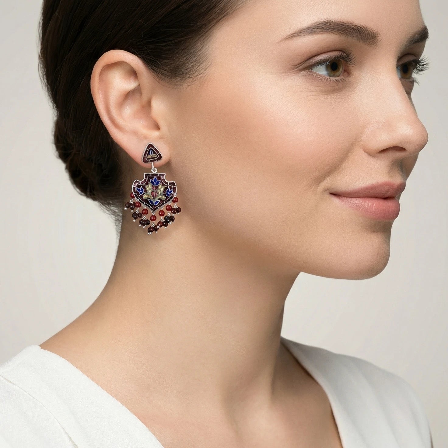 Woman wearing a decorative red-gold silver enamel earring with a neutral background