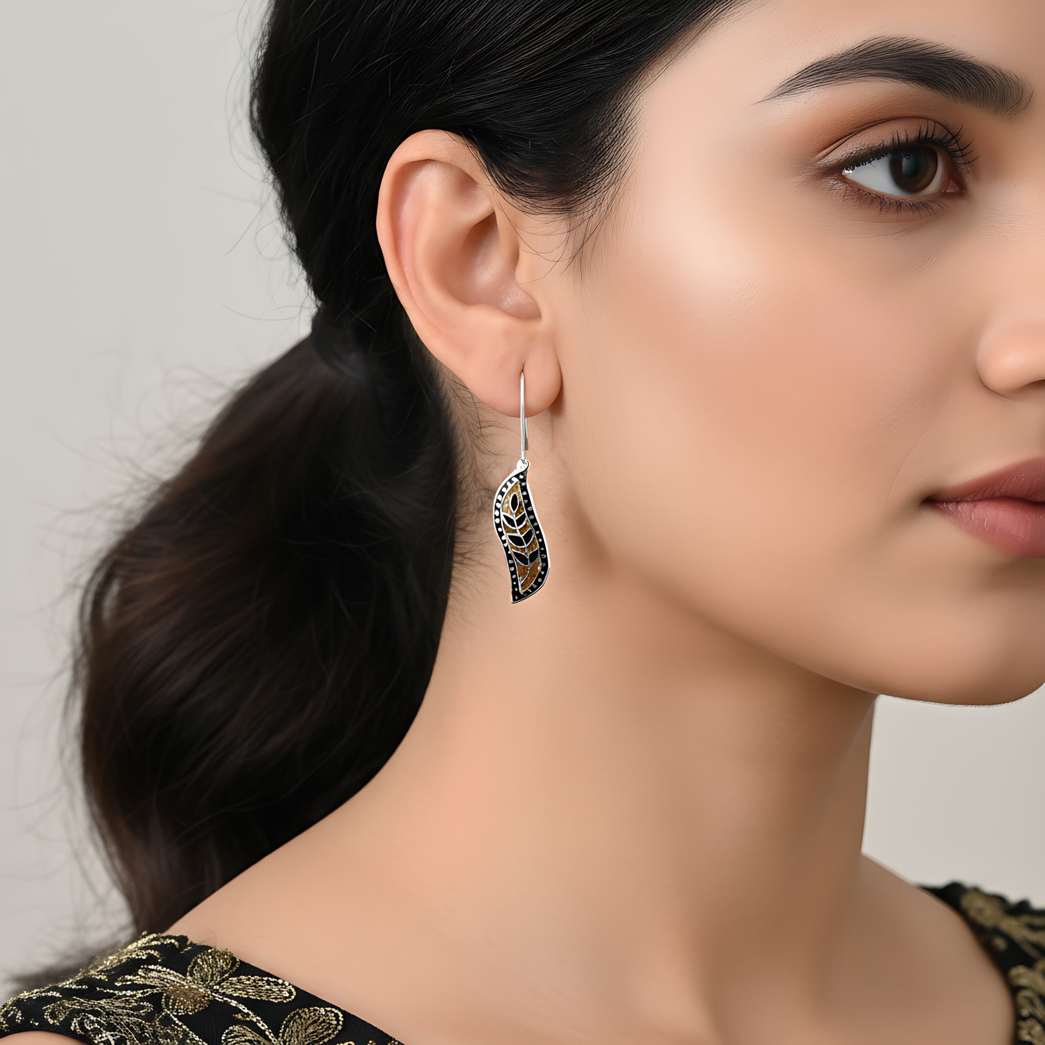 Woman wearing a decorative black-gold silver enamel earring with a neutral background