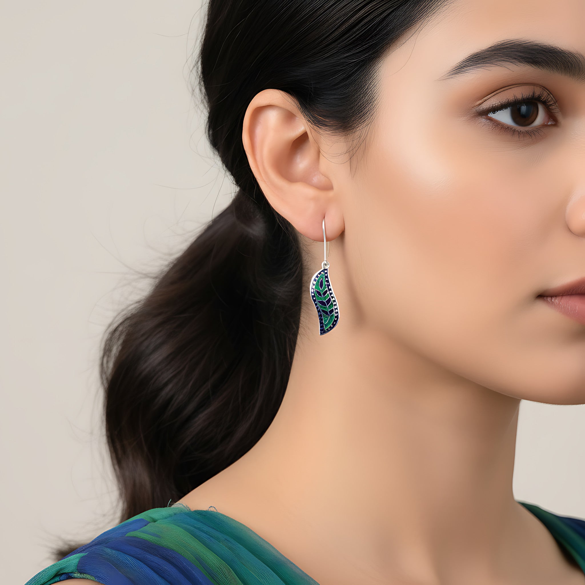 Close-up of a woman wearing a decorative blue-green silver enamel earring with a neutral background