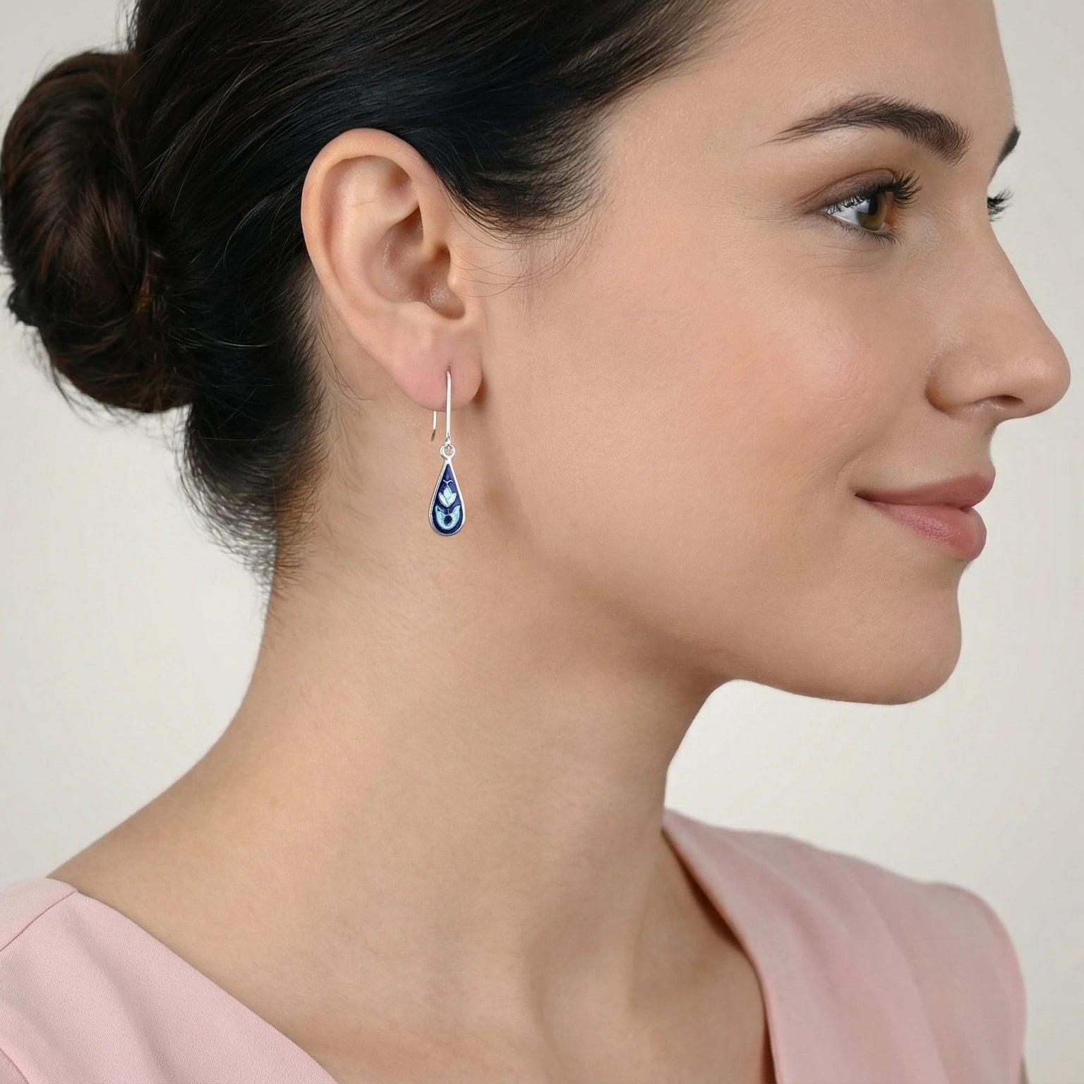 Close-up of a woman wearing a blue dewdrop silver enamel earring against a neutral background