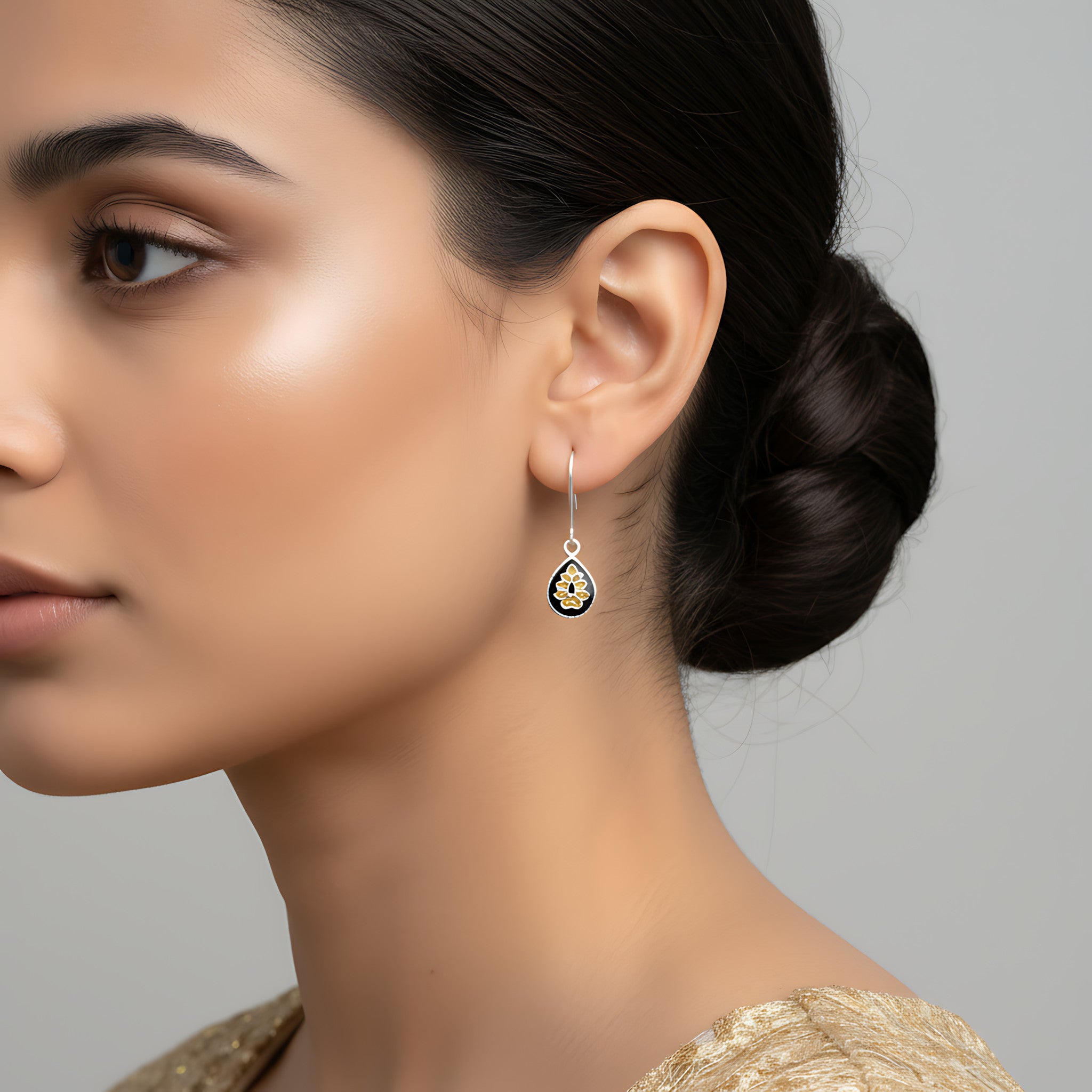 Close-up of a woman wearing a black-gold silver enamel earring against a gray background