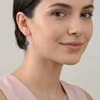 Close-up of a woman wearing a blue-green dewdrop-shaped silver enamel earring with a gray background