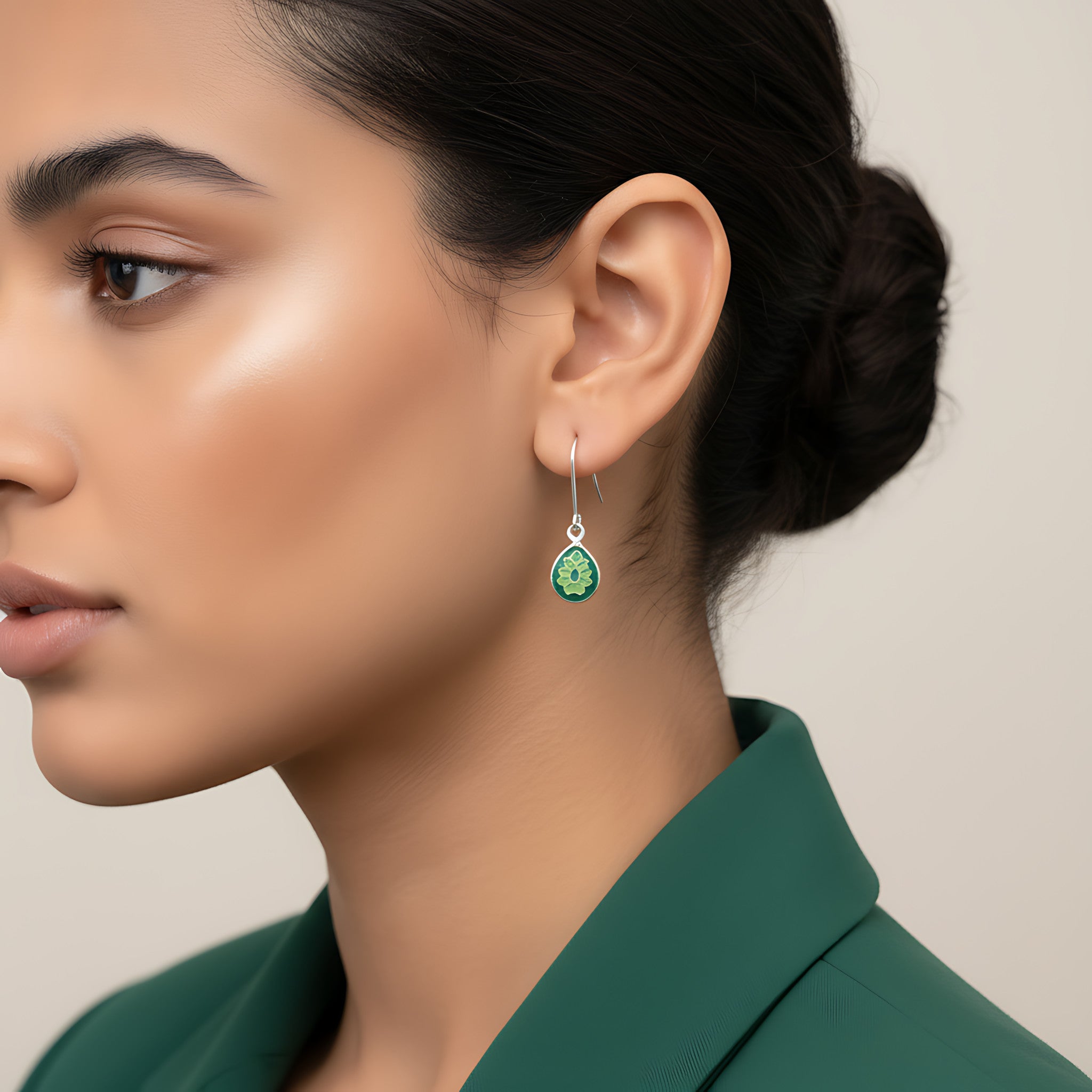 Close-up of a woman wearing a green silver enamel earring with a beige background