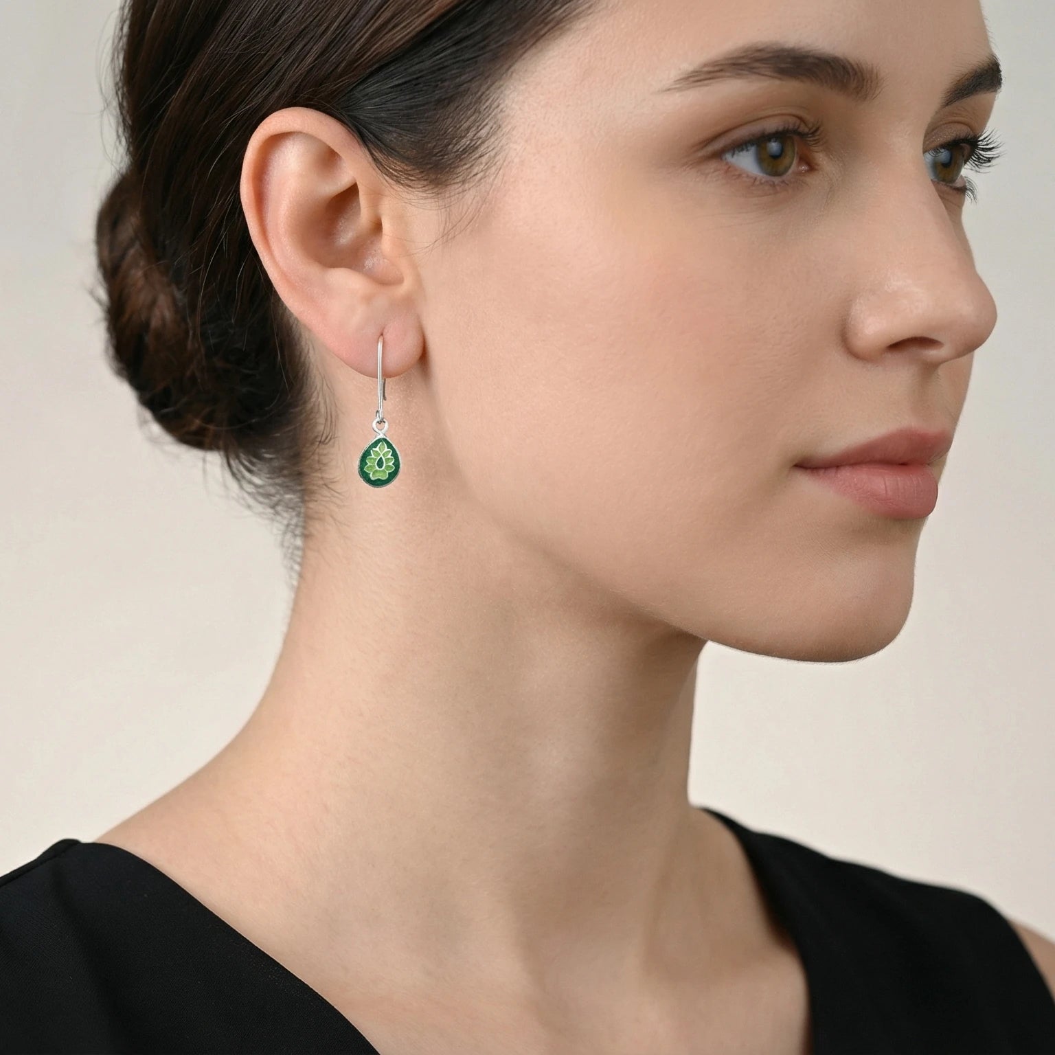 Close-up of a woman wearing a green silver enamel earring with a beige background