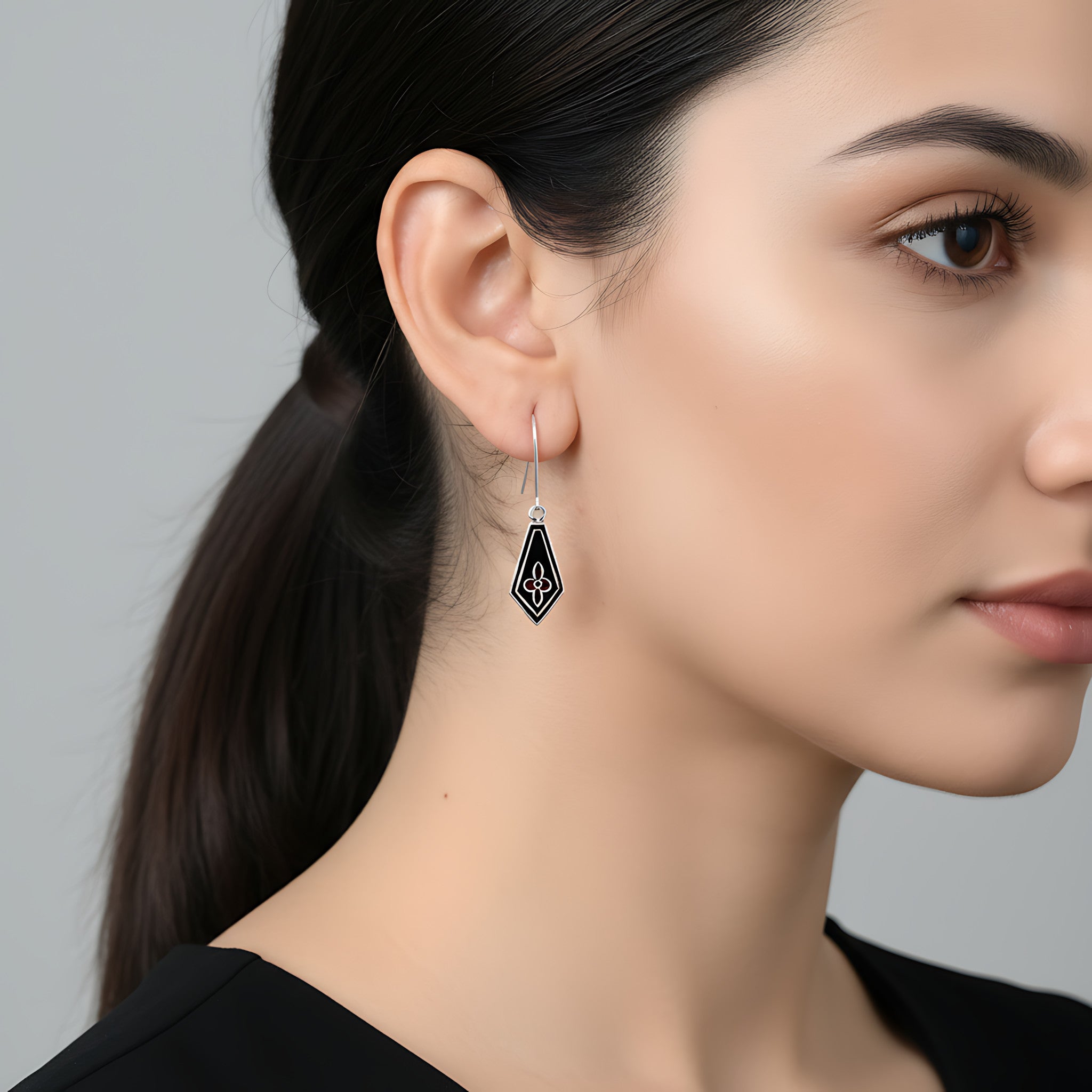 Close-up of a woman wearing a kite-shaped black enamel silver earring against a neutral background