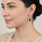 Close-up of a woman wearing a kite-shaped black enamel silver earring against a neutral background