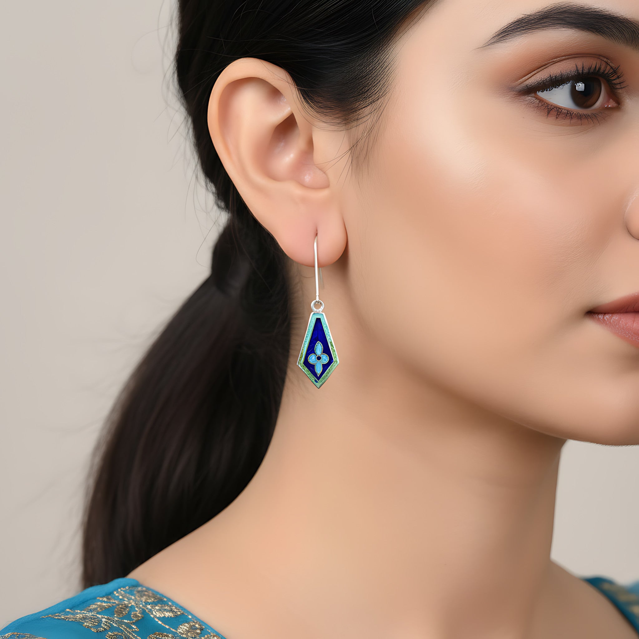 Close-up of a woman wearing a kite-shaped blue enamel silver earring against a neutral background