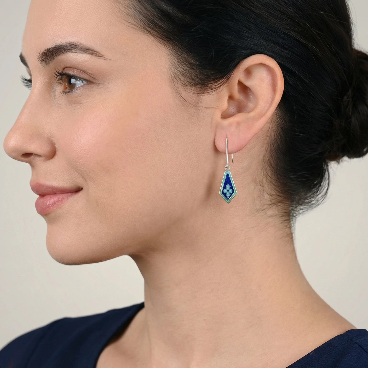 Close-up of a woman wearing a kite-shaped blue enamel silver earring against a neutral background