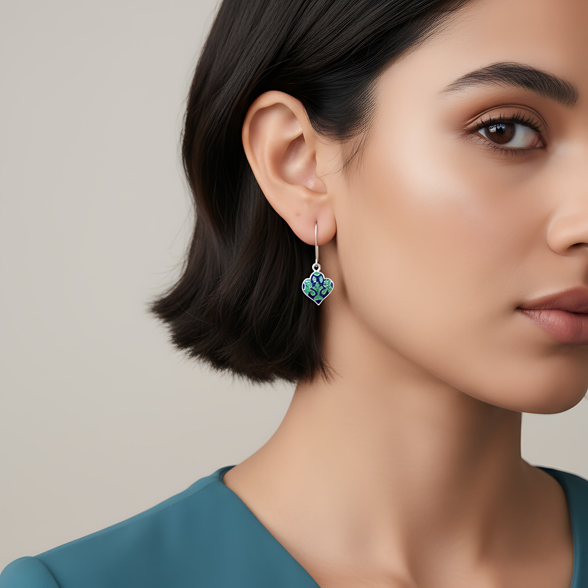Close-up of a woman wearing a pair of lantern-shaped blue-green silver enamel earrings with a neutral background