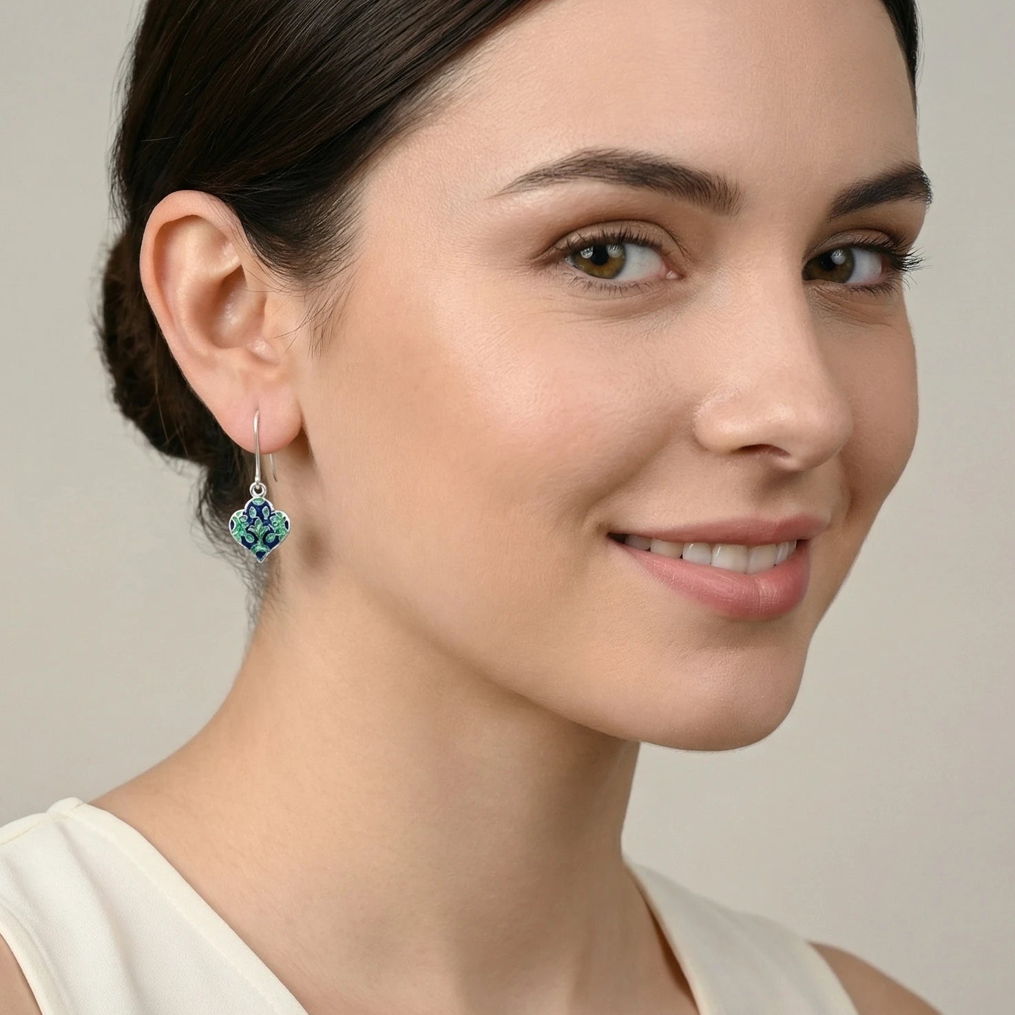 Close-up of a woman wearing a pair of lantern-shaped blue-green silver enamel earrings with a neutral background
