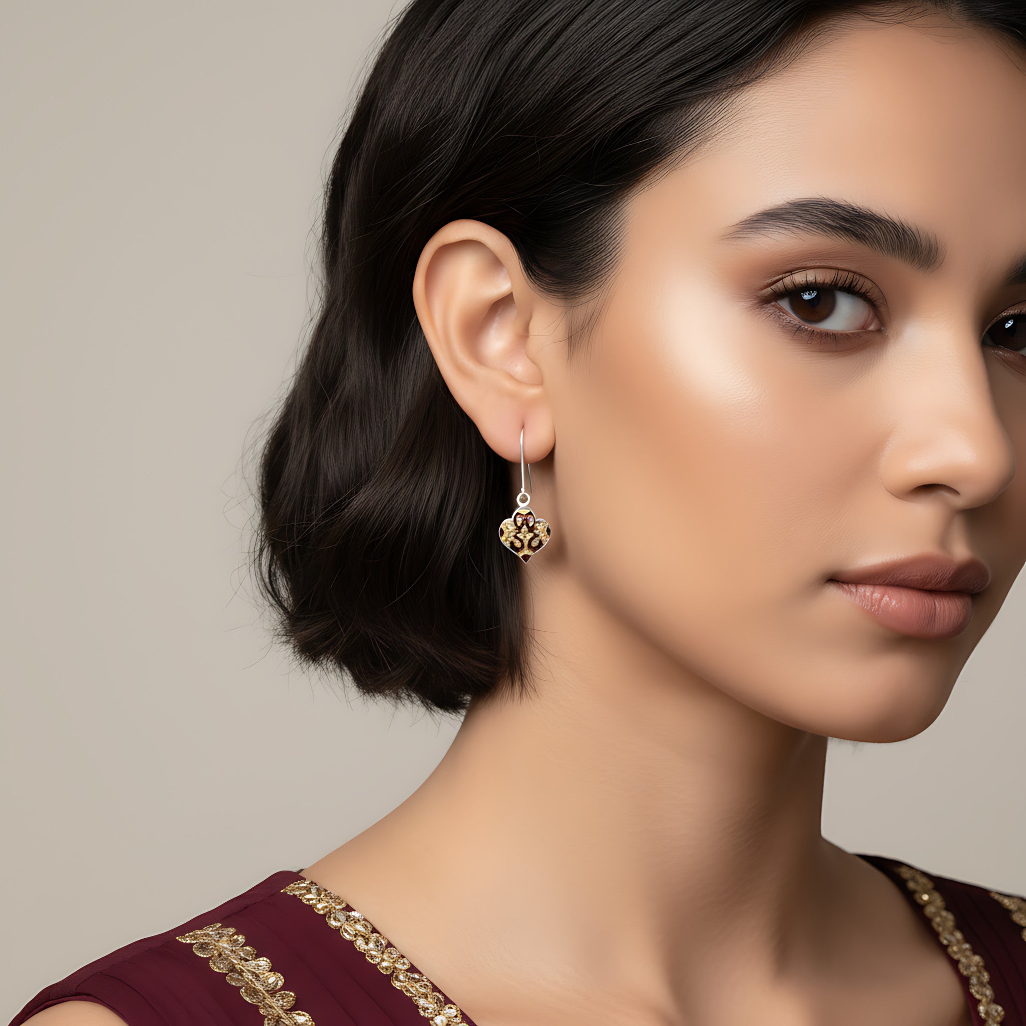 Closeup of a woman wearing maroon-gold silver enamel earrings on a plain background