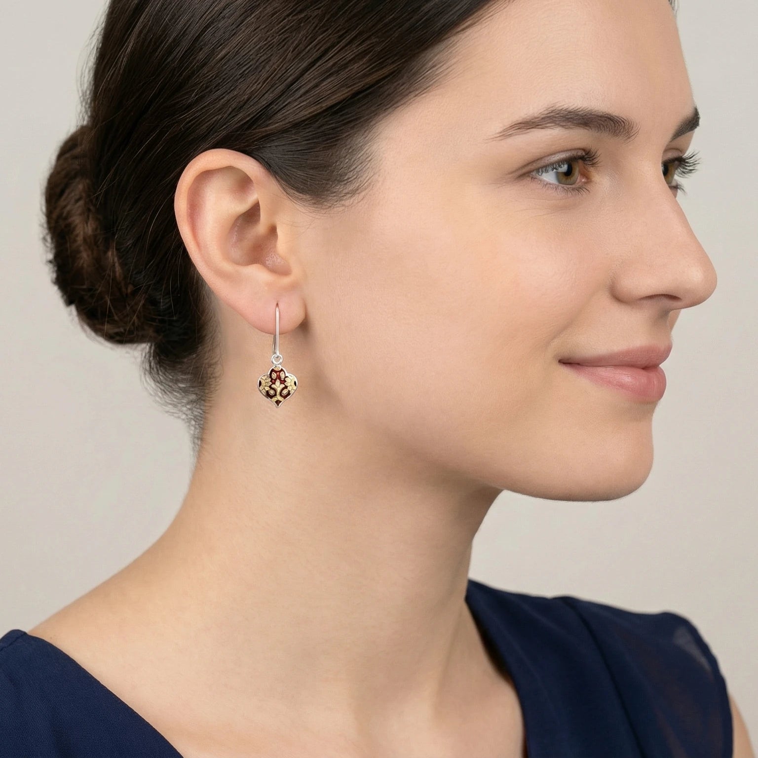 Close-up of a woman wearing a pair of lantern-shaped maroon-gold silver enamel earrings with a neutral background