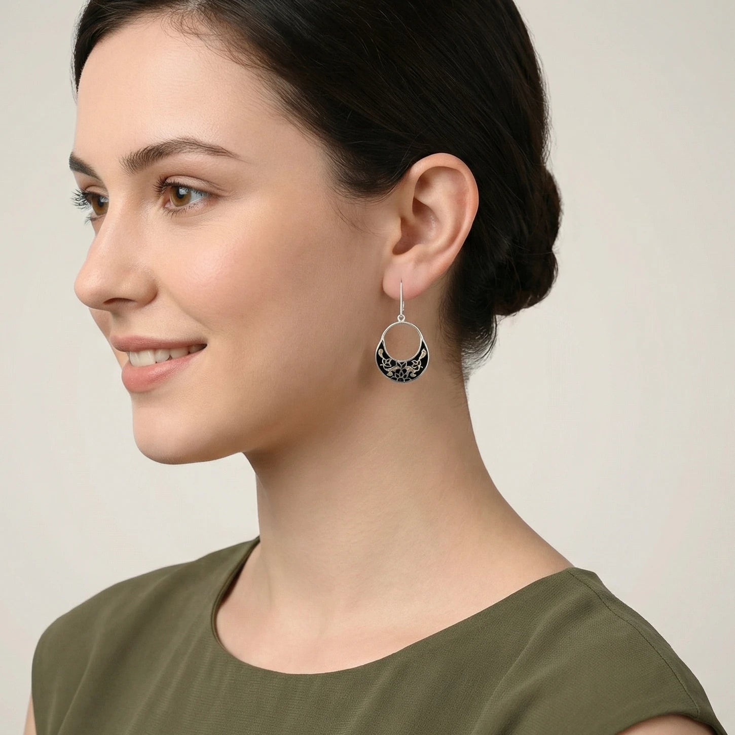 Close-up of a woman wearing a black-golden silver enamel earring against a neutral background