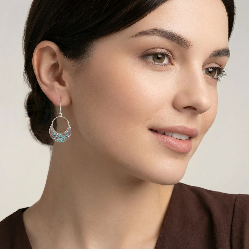 Close-up of a woman wearing a pink-turquoise silver enamel earring against a neutral background