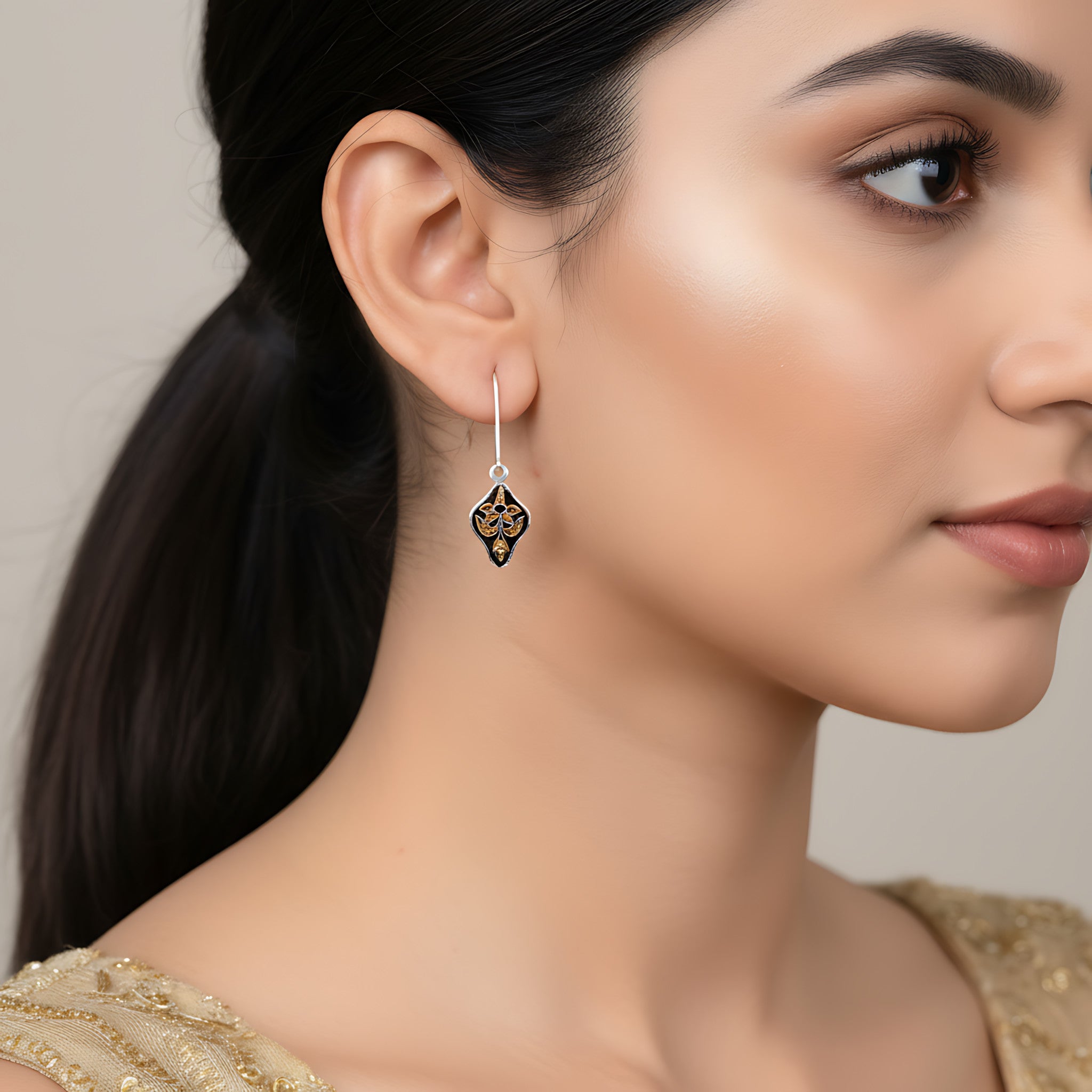 Close-up of a woman wearing a gold and black silver enamel earring against a neutral background