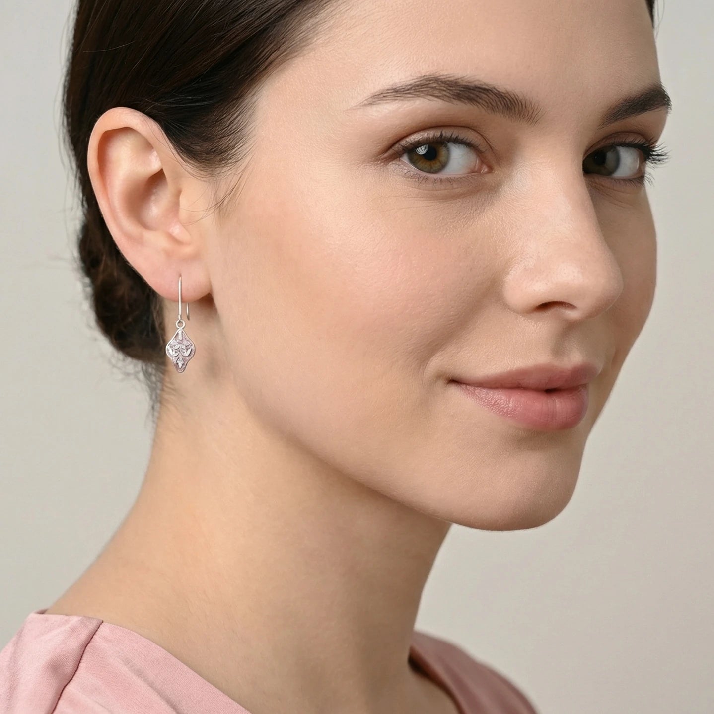 Close-up of a woman wearing a pink enamel silver earring with a neutral background