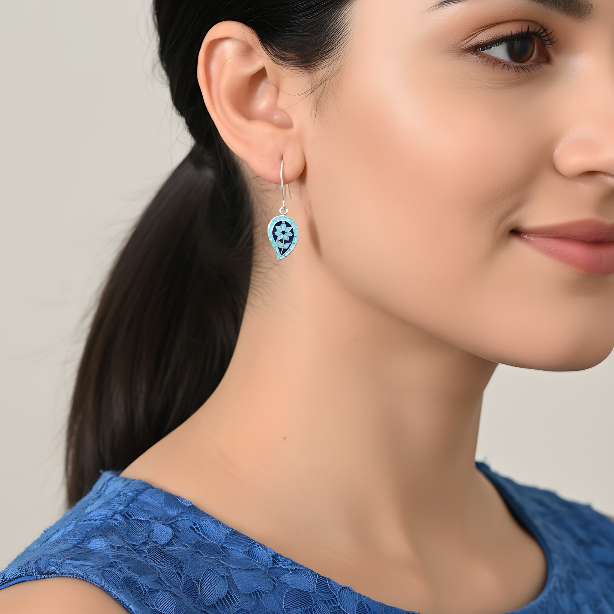 Close-up of a woman wearing blue floral silver enamel earrings with a neutral background