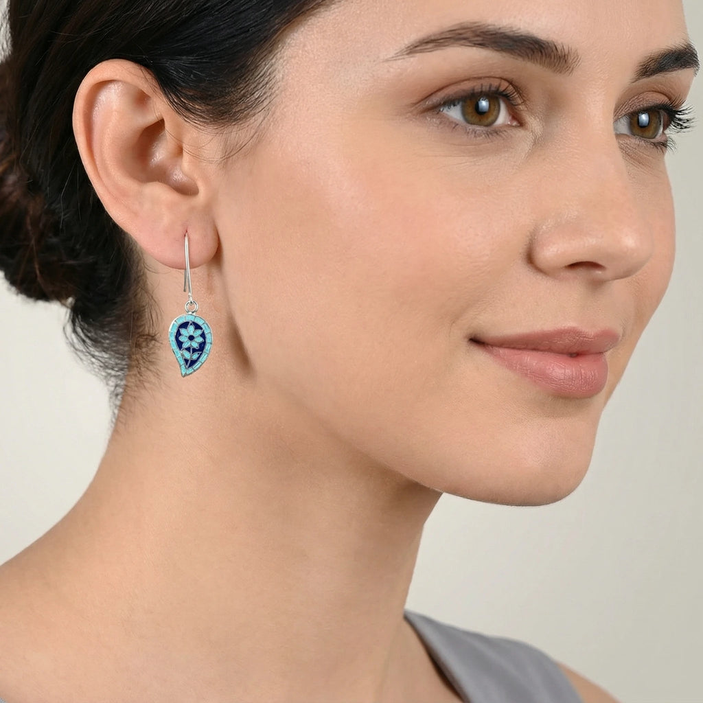 Close-up of a woman wearing a petal shaped blue enamel silver earring against a neutral background