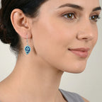 Close-up of a woman wearing a petal shaped blue enamel silver earring against a neutral background