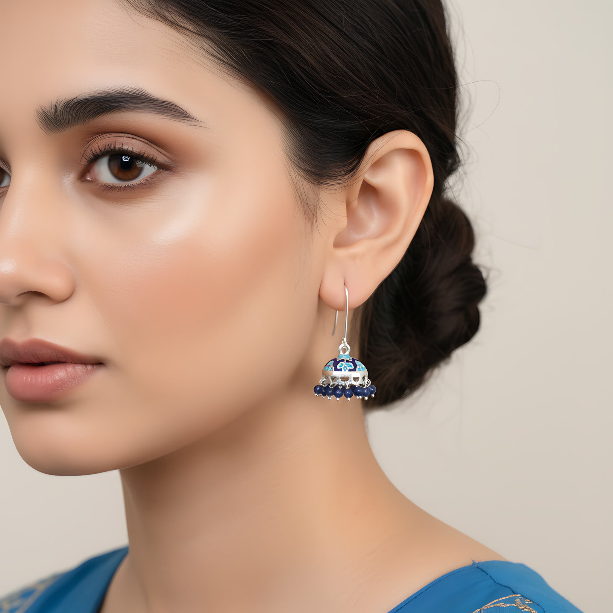 Close-up of a woman wearing a blue silver enamel silver jhumka earring with a neutral background
