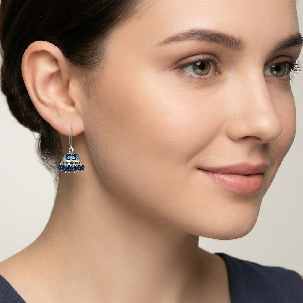 Close-up of a woman wearing a silver jhumka earring with blue enamel work.