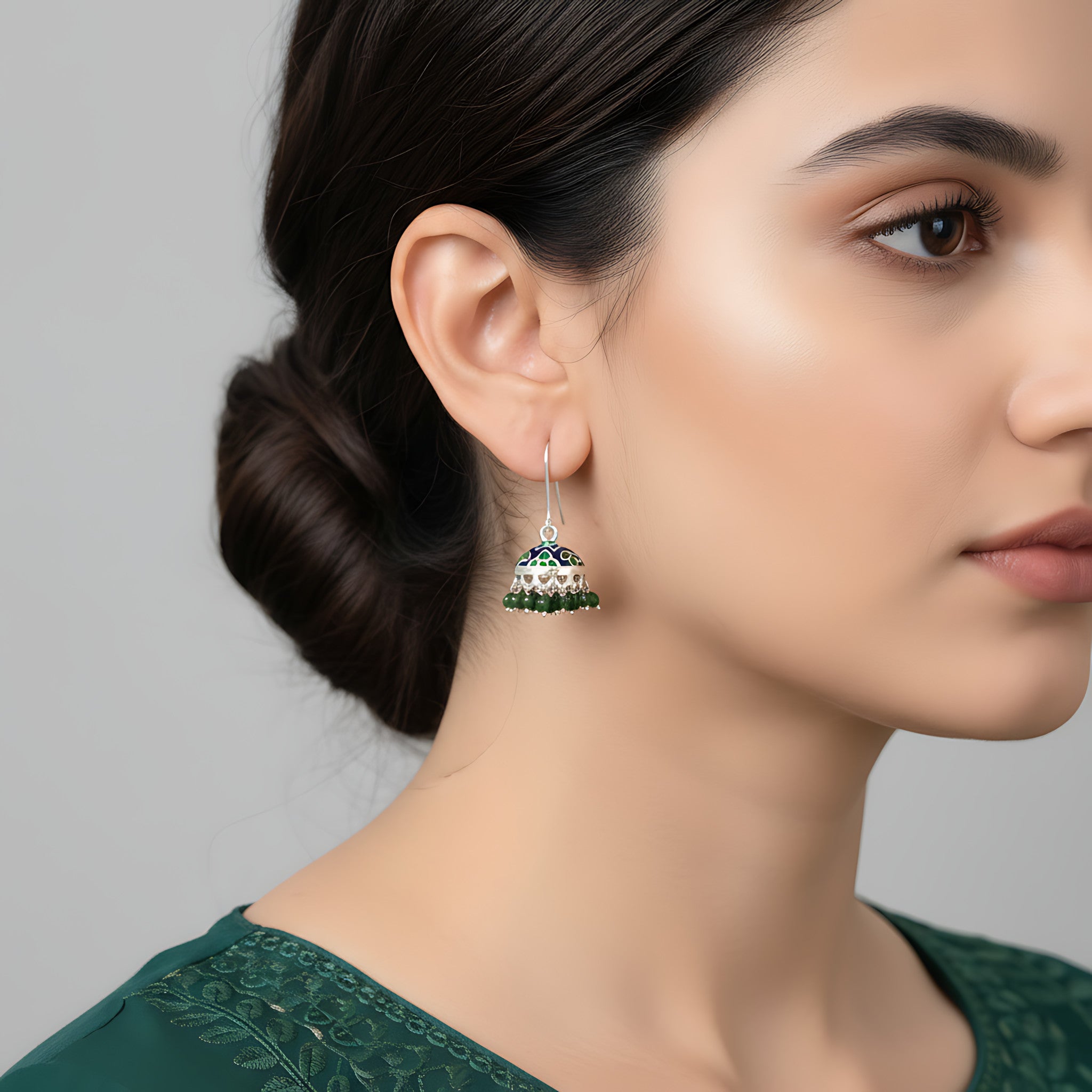 Close-up of a woman wearing a green silver enamel jhumka earring against a gray background