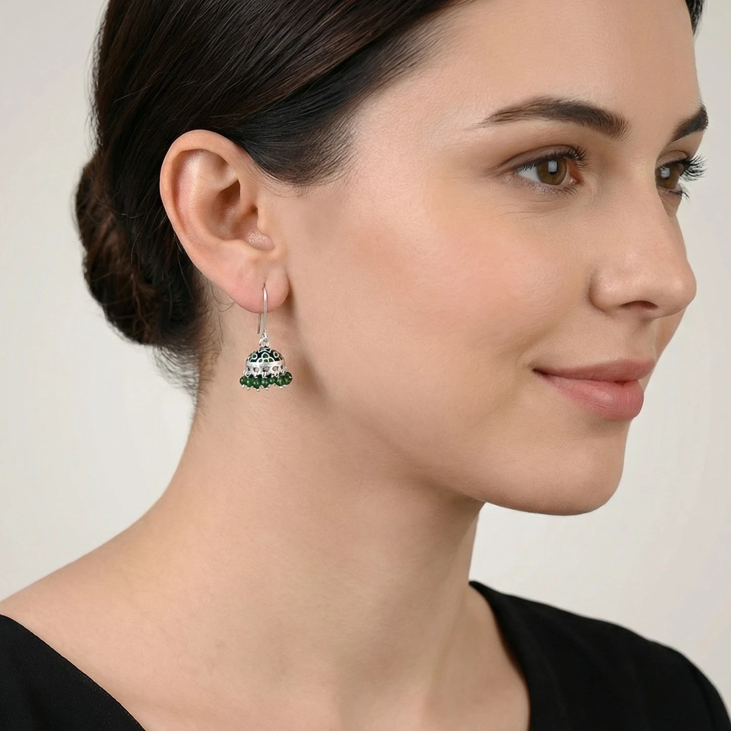 Close-up of a woman wearing a silver jhumka earring with green enamel work.