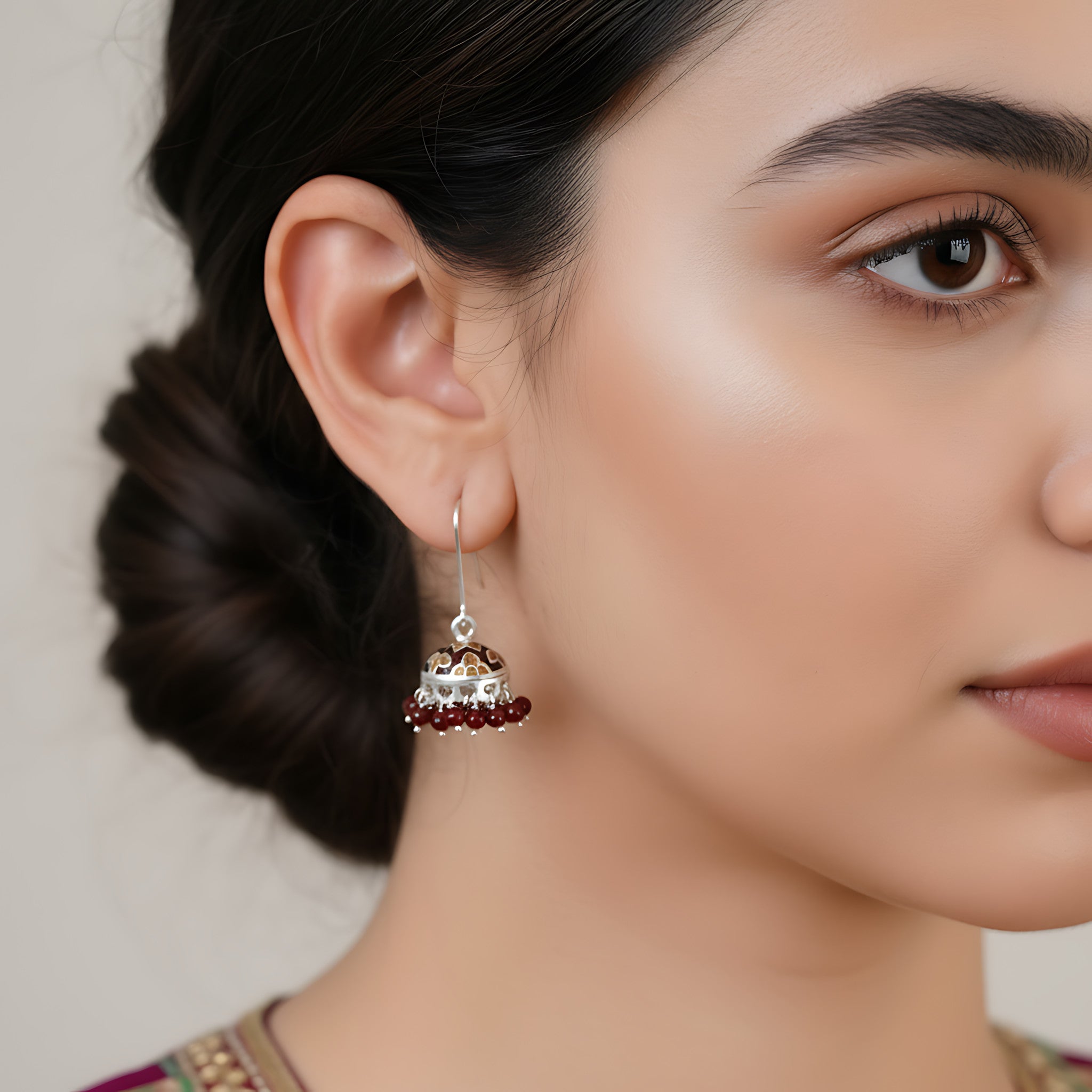 Close-up of a woman wearing a red-gold enamel silver jhumka earring with a neutral background
