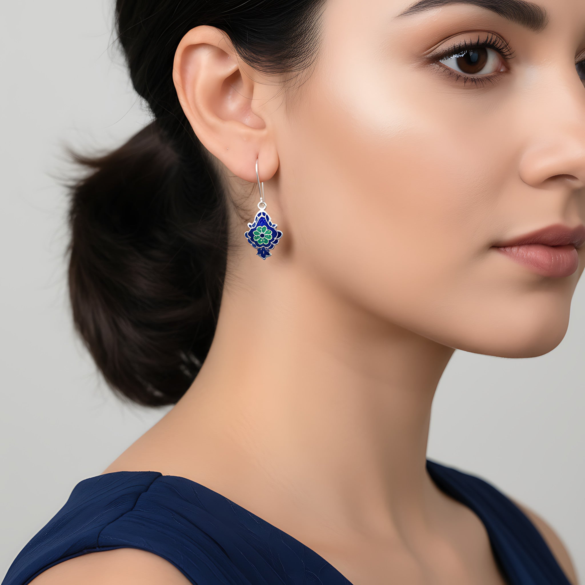Close-up of a woman wearing a blue and green enamel silver earring against a neutral background