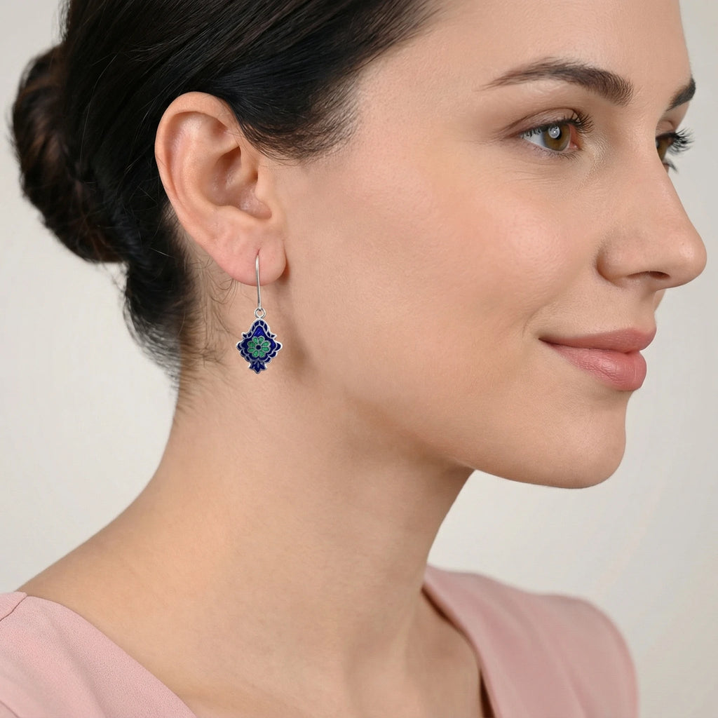 Close-up of a woman wearing an ornate blue-green enamel silver earring on a plain background