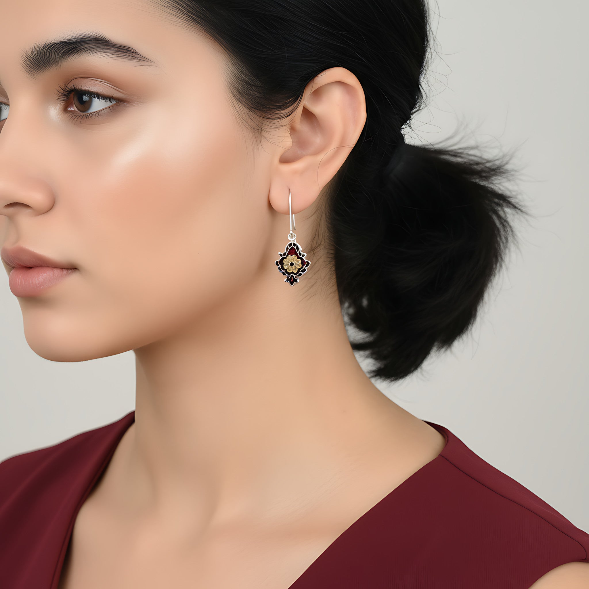 Close-up of a woman wearing an ornate maroon-gold enamel silver earring on a plain background