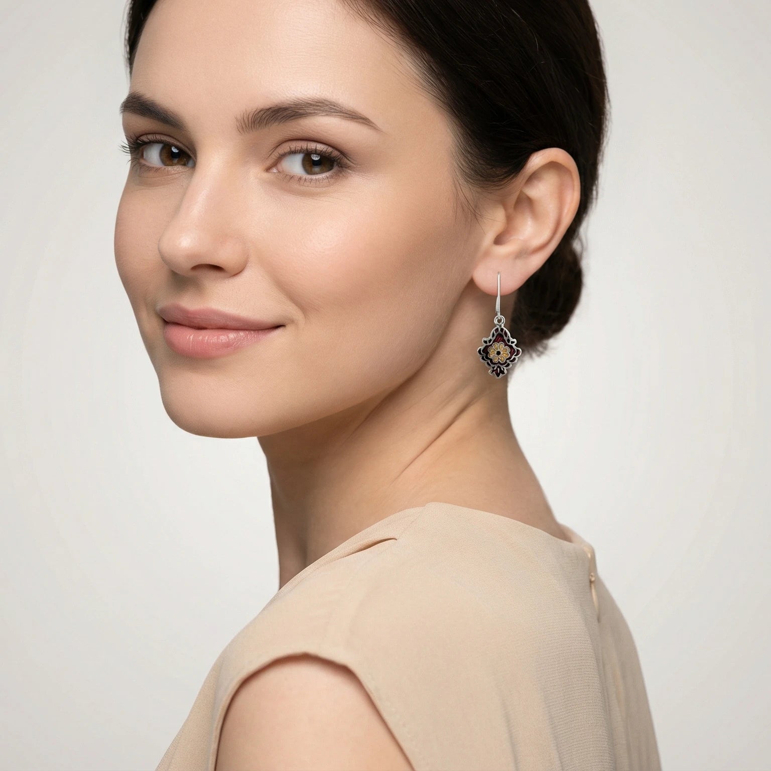 Close-up of a woman wearing an ornate maroon-gold enamel silver earring on a plain background