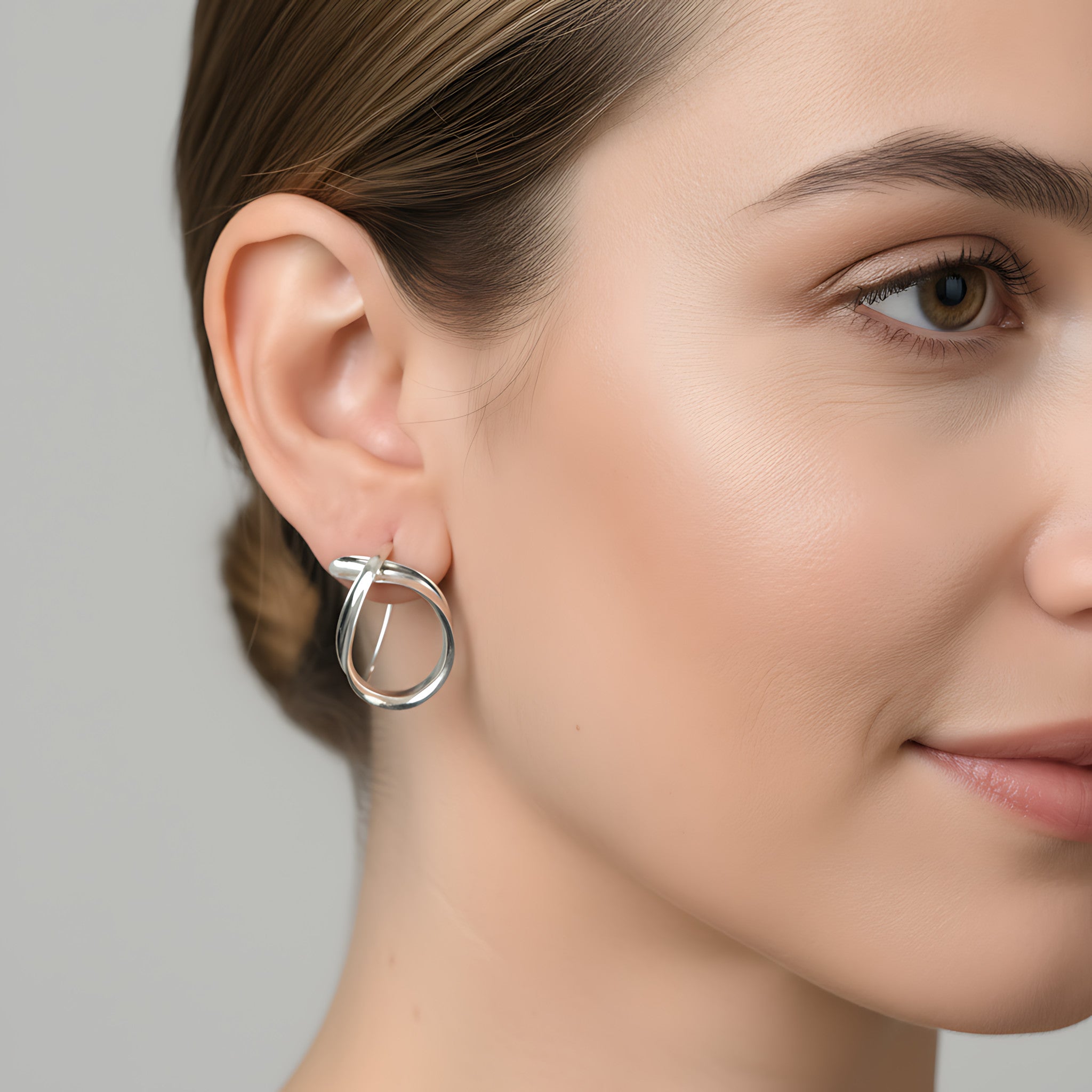 Close-up of a woman wearing a shiny silver dangle earring against a neutral background