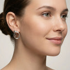 Close-up of a woman wearing a shiny silver dangle earring against a neutral background