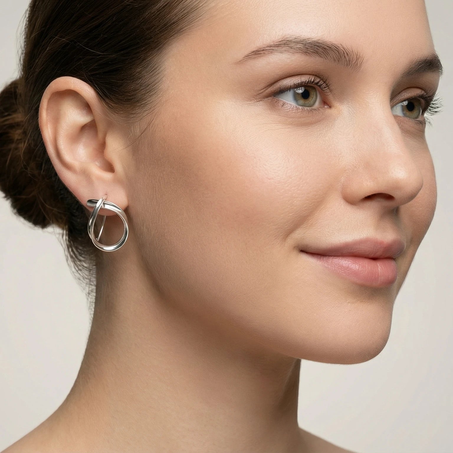 Close-up of a woman wearing a shiny silver dangle earring against a neutral background