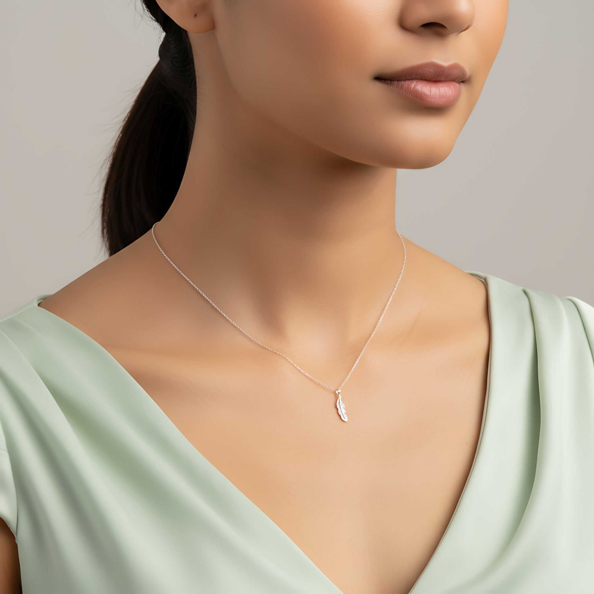 Closeup of a female wearing a silver necklace with a small feather pendant against a neutral background