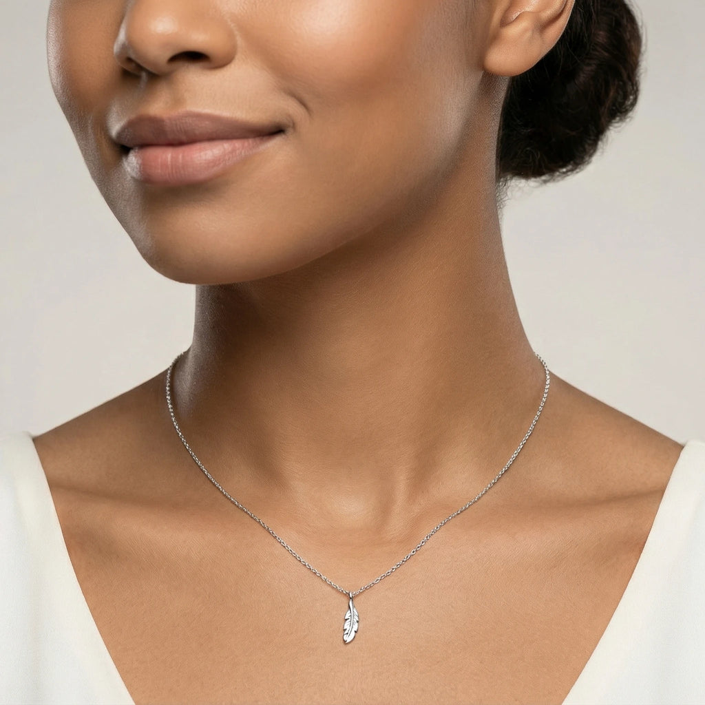 Closeup of a female wearing a silver necklace with a small feather pendant against a neutral background