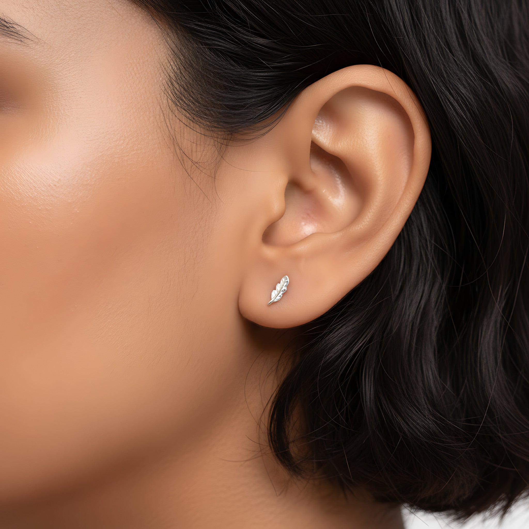 Close-up of an ear wearing a silver feather-shaped stud earring