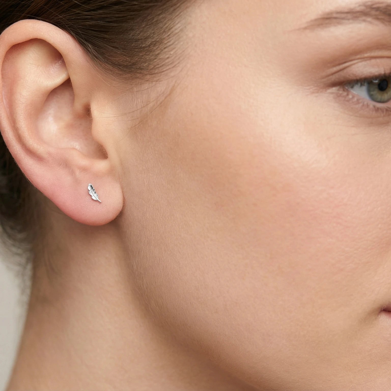 Close-up of an ear wearing a silver feather-shaped stud earring