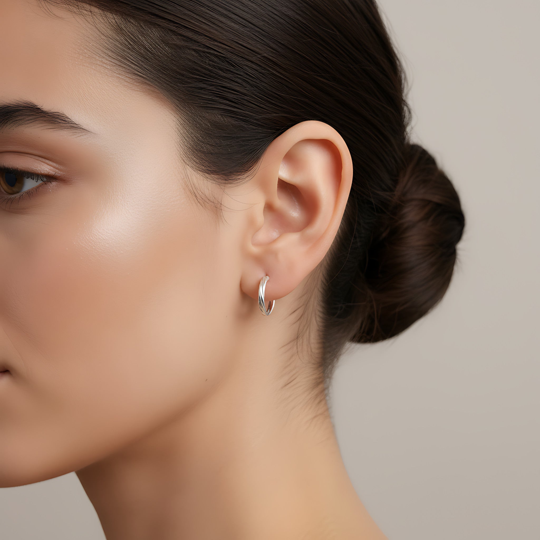 Close-up of a woman's ear wearing a silver half hoop stud earring with a neutral background