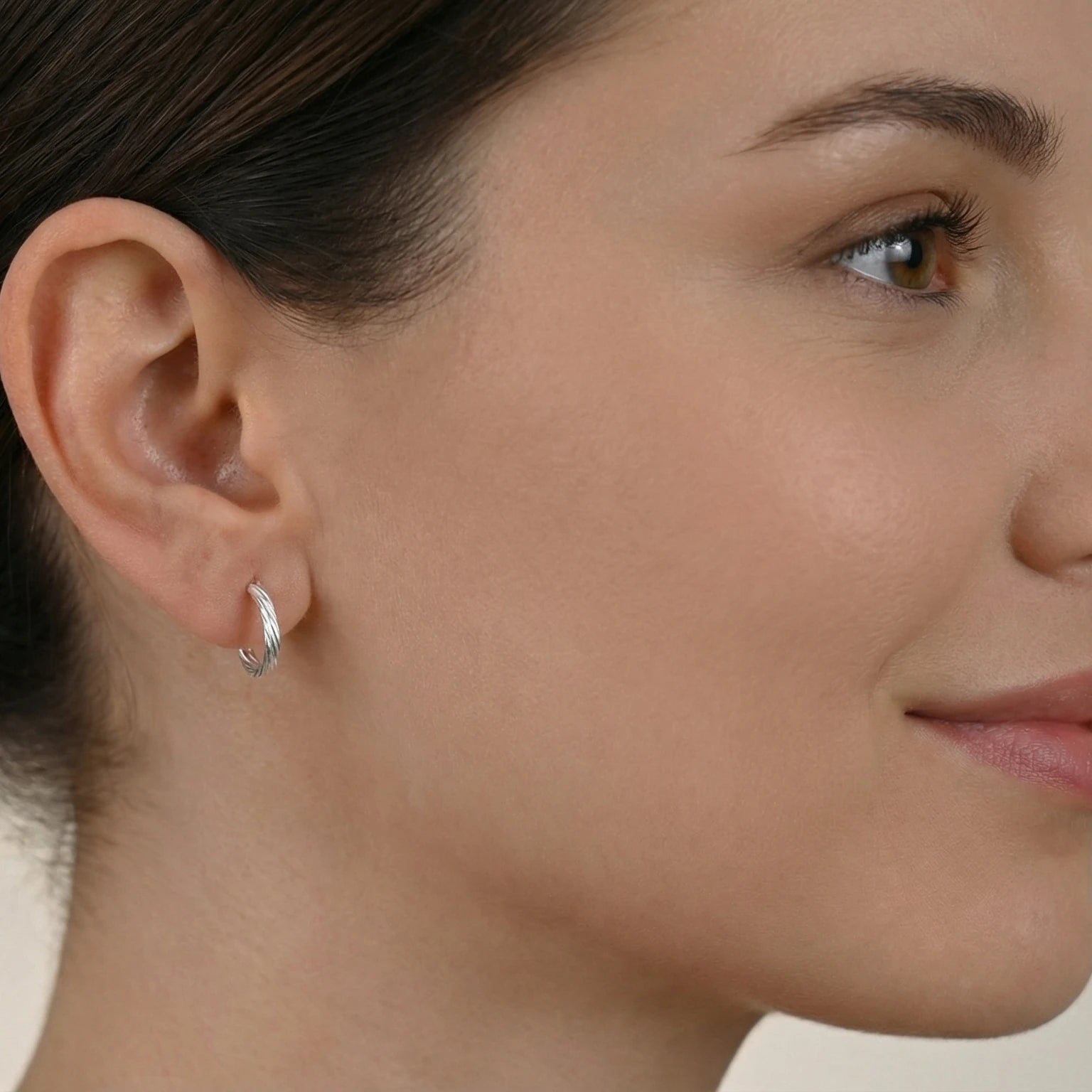Close-up of a woman's ear wearing a silver half hoop stud earring with a neutral background