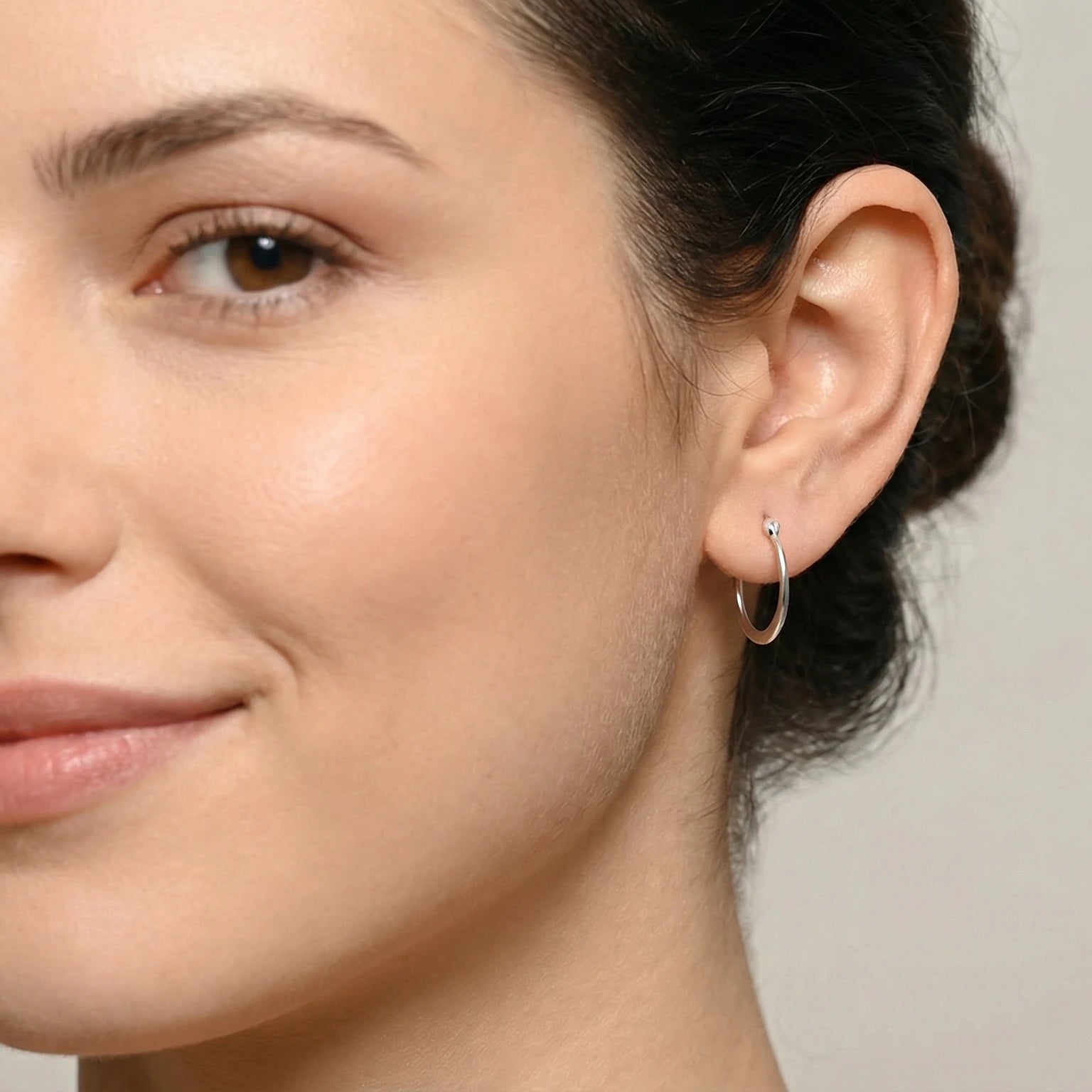 Close-up of a woman wearing a Silver Flat French Lock Hoop Earring against a neutral background