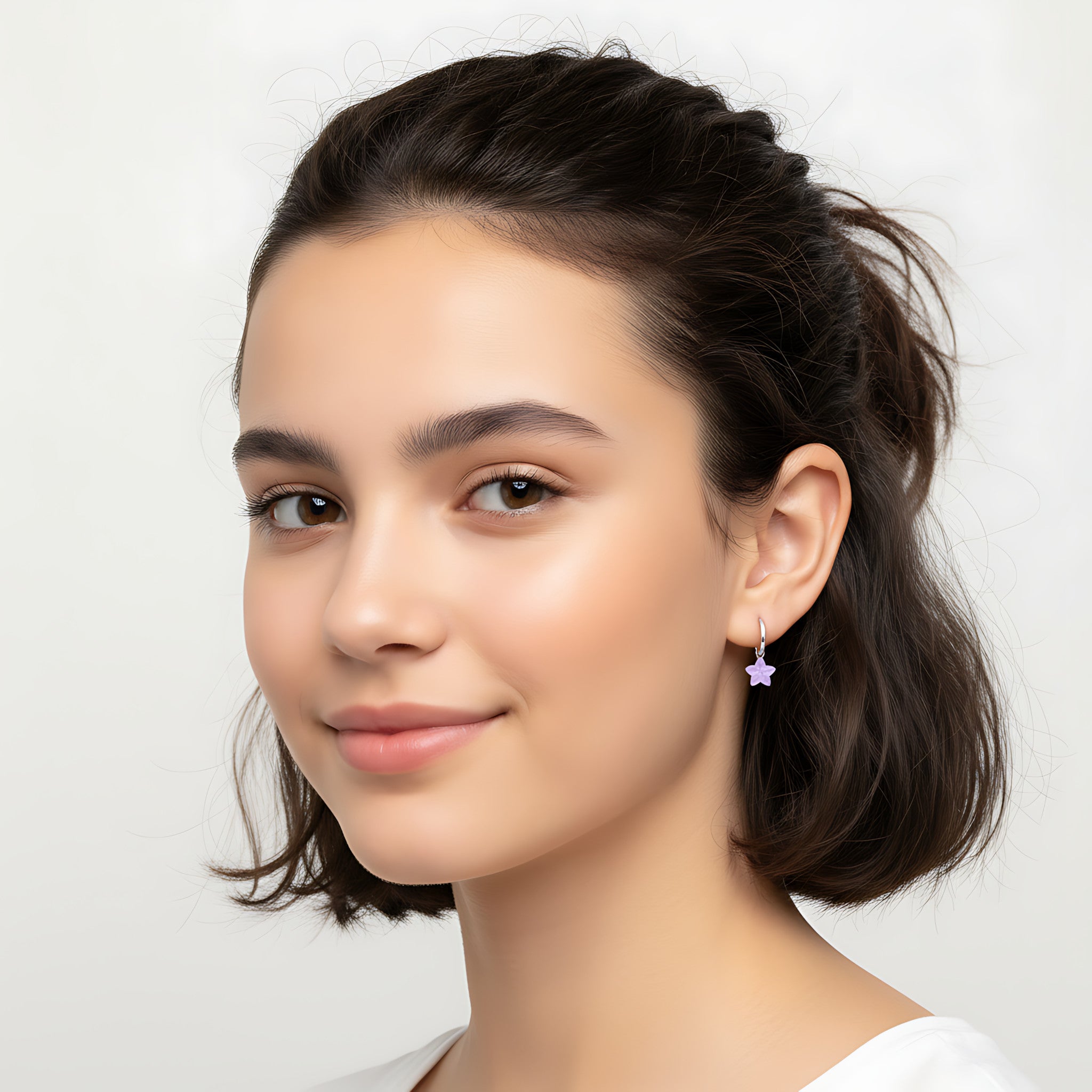 Closeup of a girl wearing a silver hoop earrings with a flower charm on a plain background