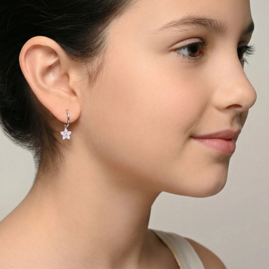 Closeup of a girl wearing a silver hoop earrings with a flower charm on a plain background