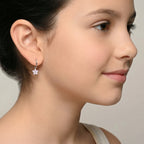 Closeup of a girl wearing a silver hoop earrings with a flower charm on a plain background