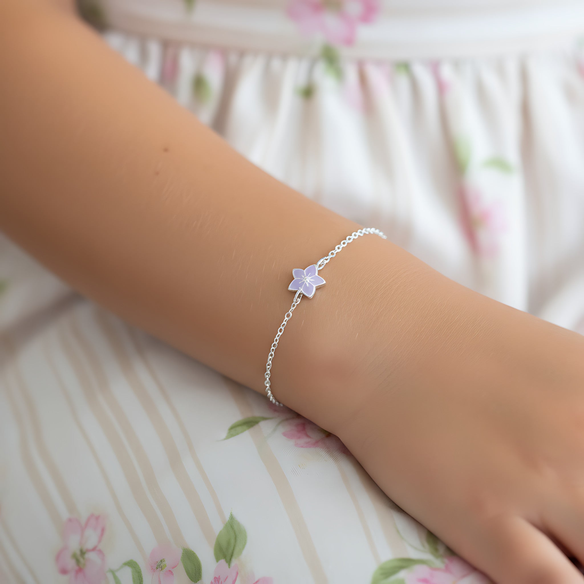 Silver bracelet with a flower charm on a wrist against a floral background